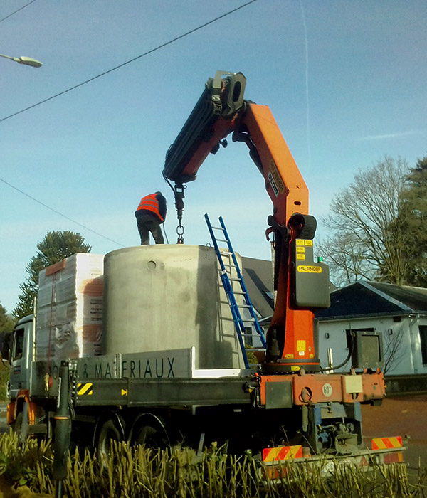 Op&eacute;rateur installant une cuve en b&eacute;ton &agrave; l&rsquo;aide d&rsquo;une grue hydraulique mont&eacute;e sur un camion lors de travaux d&rsquo;am&eacute;nagement.